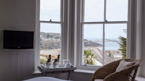 A hotel room with a large window offering a view of the sea and hills. - Headland House Luxury B&B (St Ives)