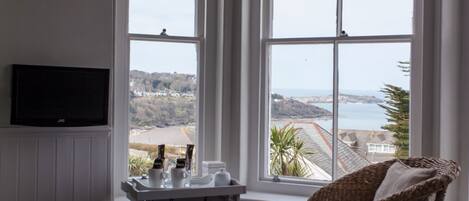 A hotel room with a large window offering a view of the sea and hills.
