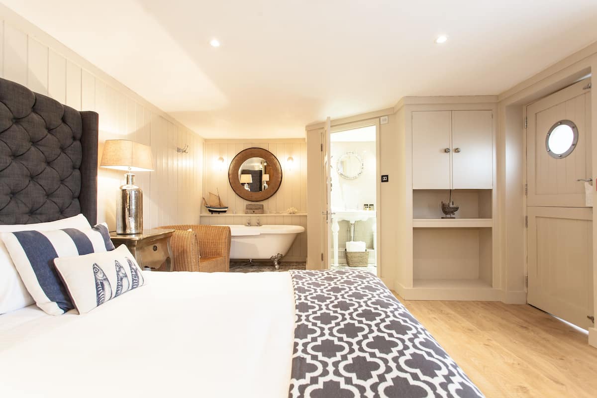 Een slaapkamer met een groot bed, een nachtkastje, een lamp, een stoel, een badkamer met een bad en een kledingkast.