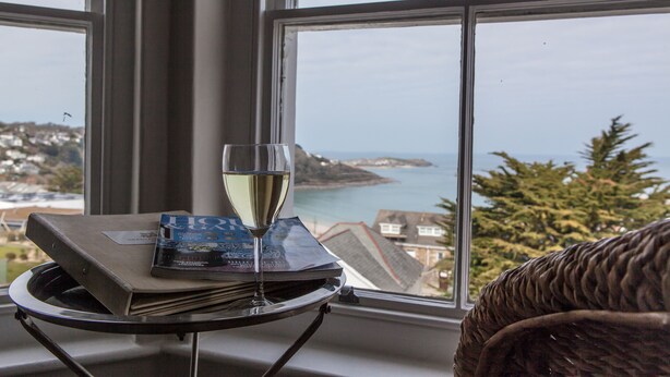 A table with a glass of white wine and a magazine, positioned by a window overlooking a coastal view. - Headland House Luxury B&B (St Ives)