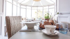 A breakfast table with croissants, a bowl, a cup, and a glass of water in a bright room with large windows. - Headland House Luxury B&B (St Ives)