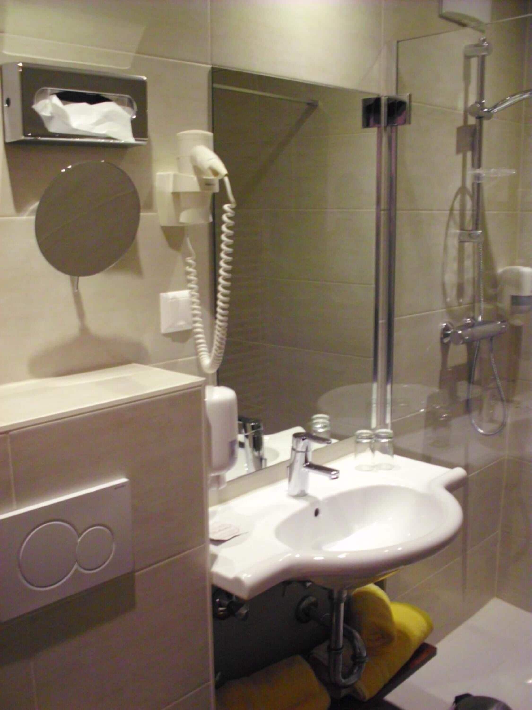 A bathroom with a sink, mirror, towel dispenser, and a shower.