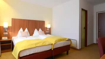 A hotel room with a double bed, two bedside tables with lamps, a wooden headboard, a red chair, and a door to the right.