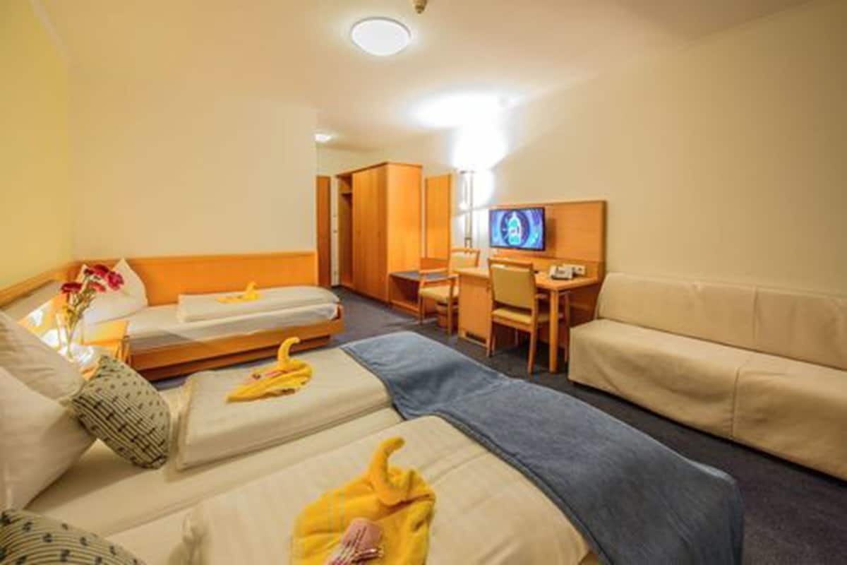 A hotel room with two beds, a sofa, a desk, and a television.