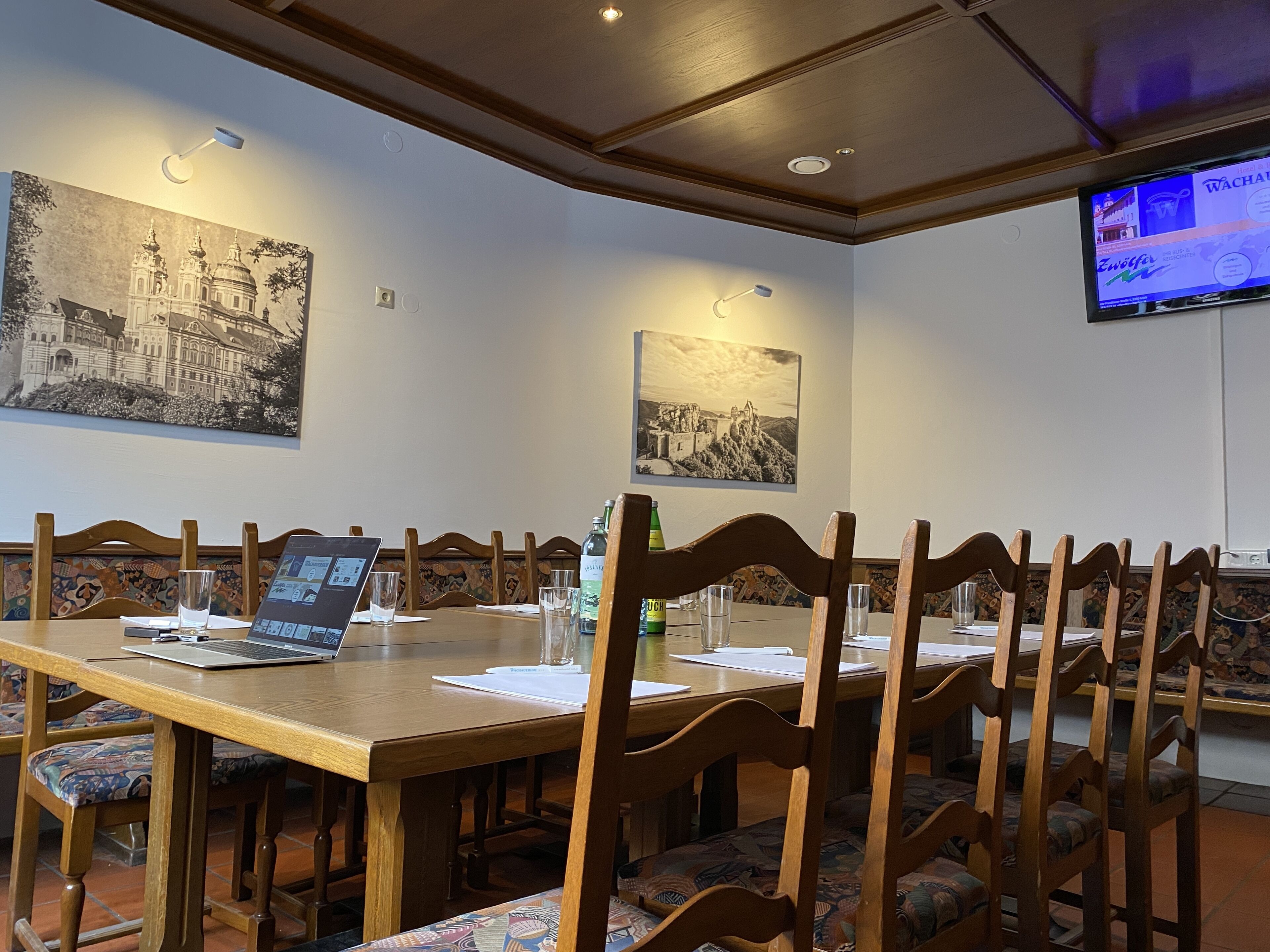 Een vergaderruimte met een lange tafel, stoelen, een laptop en een televisie aan de muur.