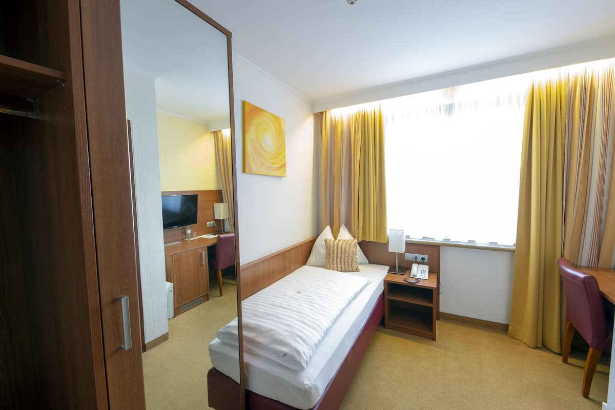 A hotel room with a bed, a desk, a chair, a TV, and a window with curtains.