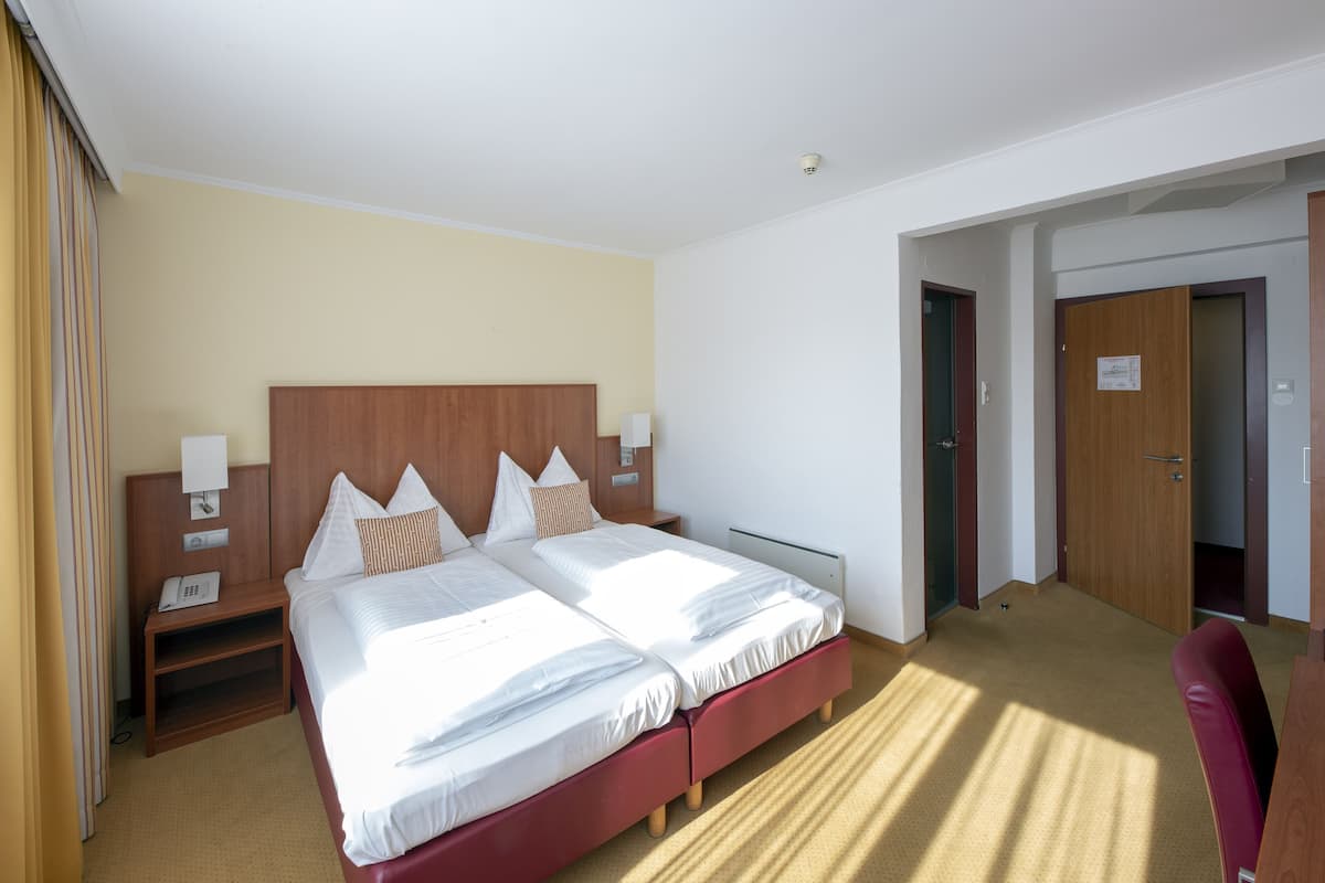 A hotel room with a double bed, a wooden headboard, bedside tables with lamps, and a red chair.
