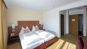 Habitación de hotel con cama doble, cabecera de madera, mesitas de noche con lámparas y una silla roja.