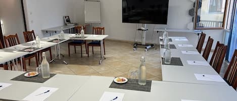 A conference room with long tables, chairs, a whiteboard, a TV screen, and a window.
