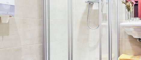 A modern bathroom with a glass-enclosed shower, a toilet, and a sink with a vase of flowers.