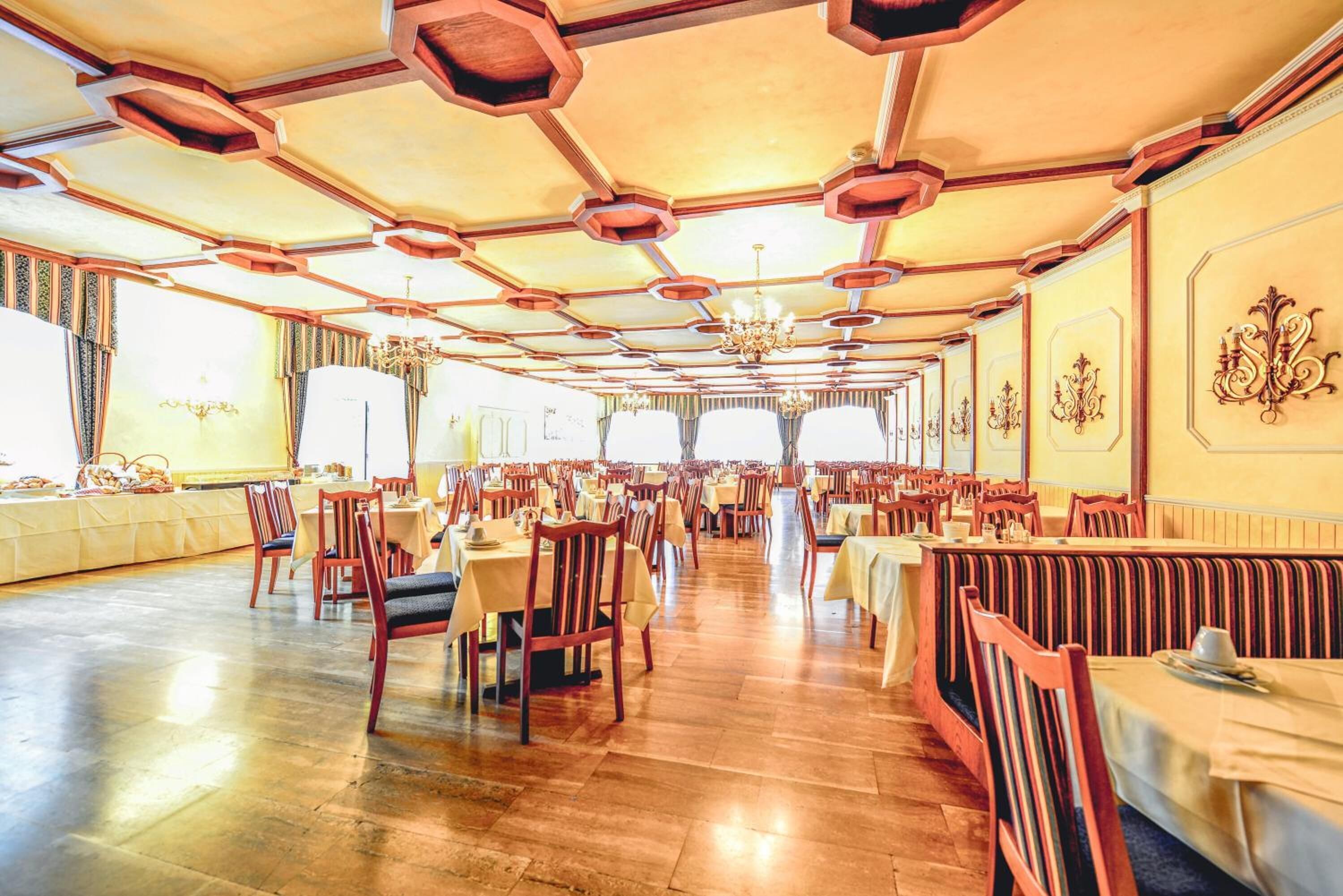 A spacious dining hall with hexagonal ceiling patterns, wooden flooring, and multiple tables and chairs.