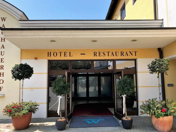 A hotel entrance with a sign reading "HOTEL - RESTAURANT" and a blue wheelchair accessibility symbol on the mat.