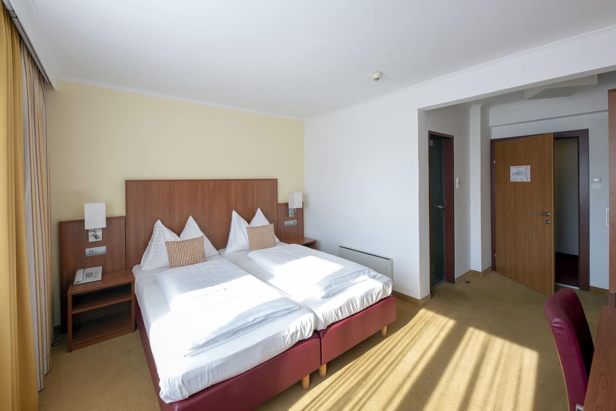 A hotel room with a double bed, bedside tables, a wardrobe, and a door leading to another room.