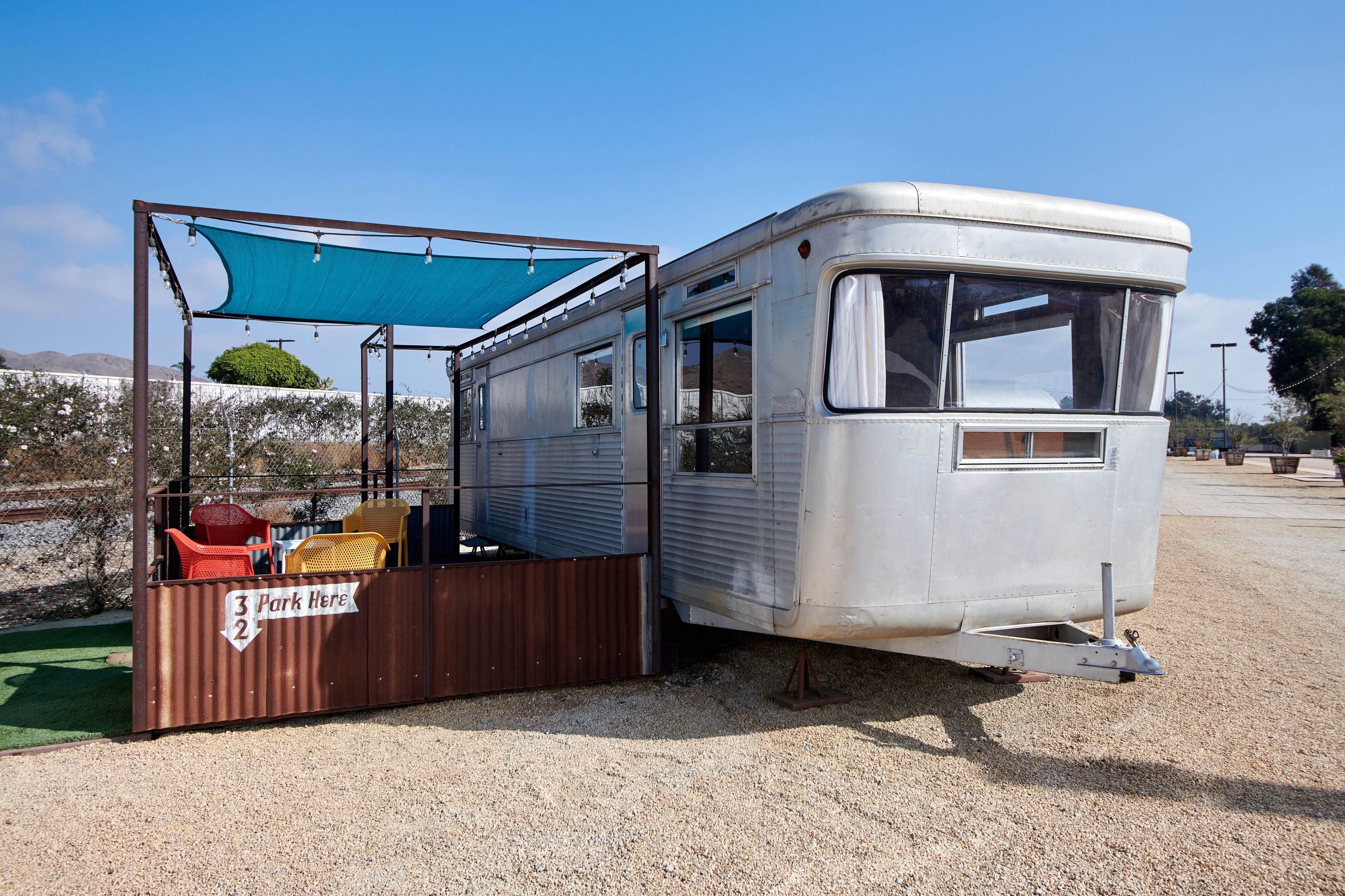 A vintage camper parked next to a shaded picnic area with a sign indicating parking spots 3 and 2.
