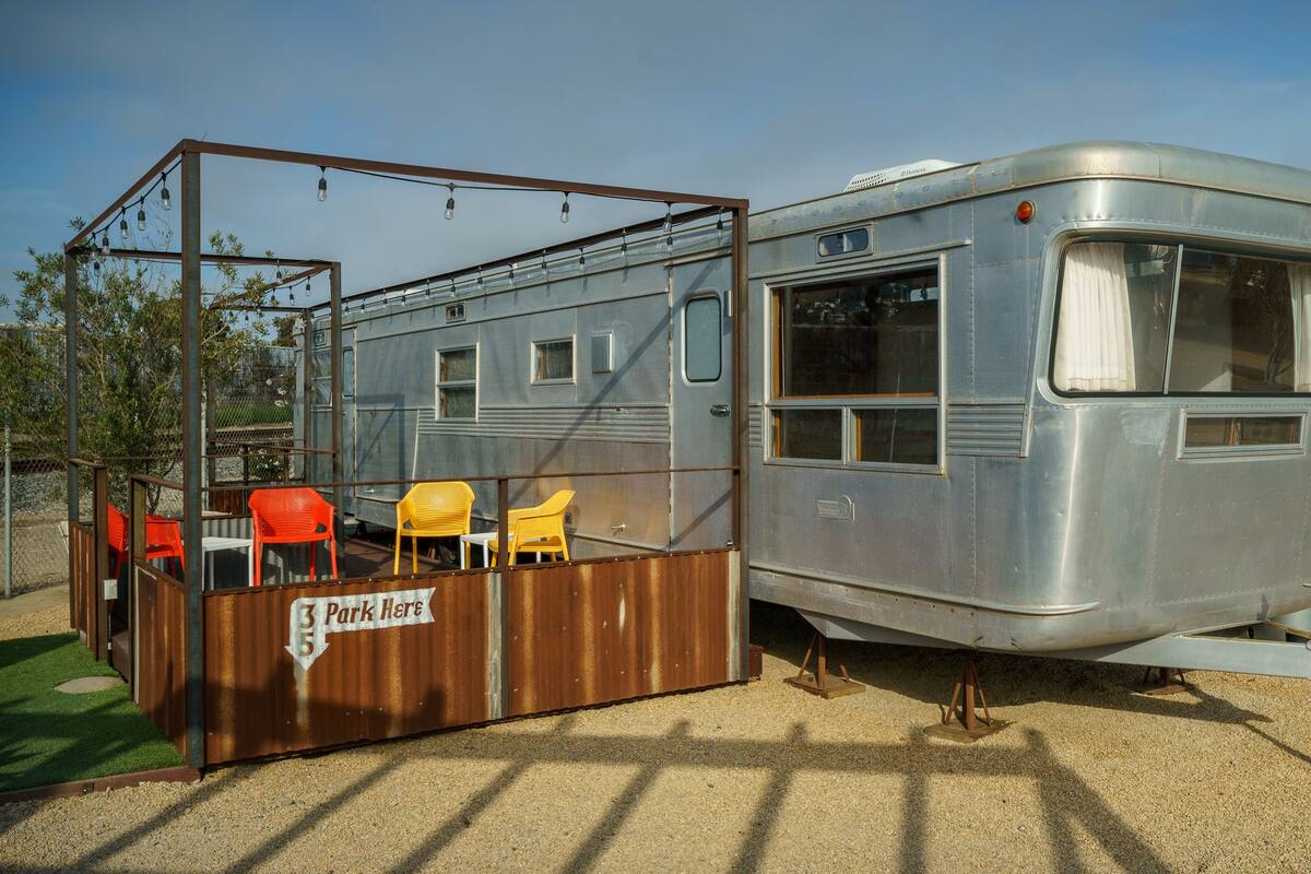 A vintage RV with a small attached structure featuring outdoor seating.