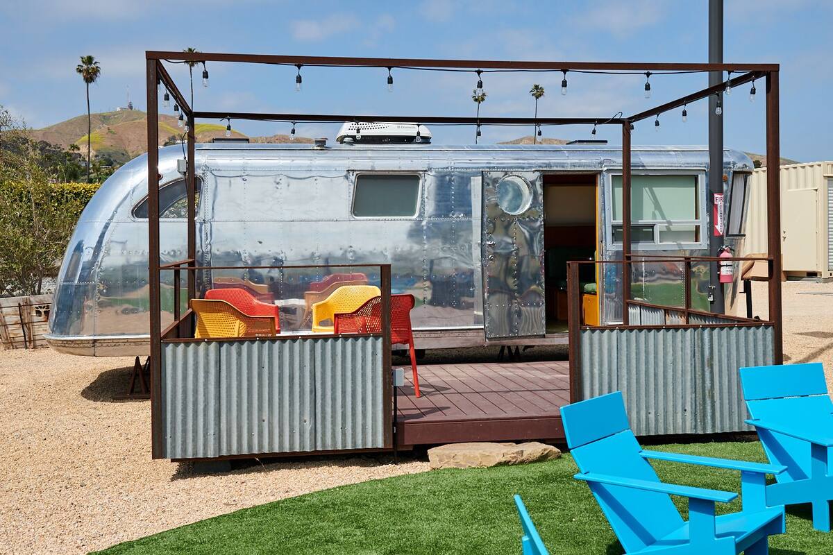 A transparent RV with a deck area featuring red and yellow chairs, a small table, and a blue lounge chair.