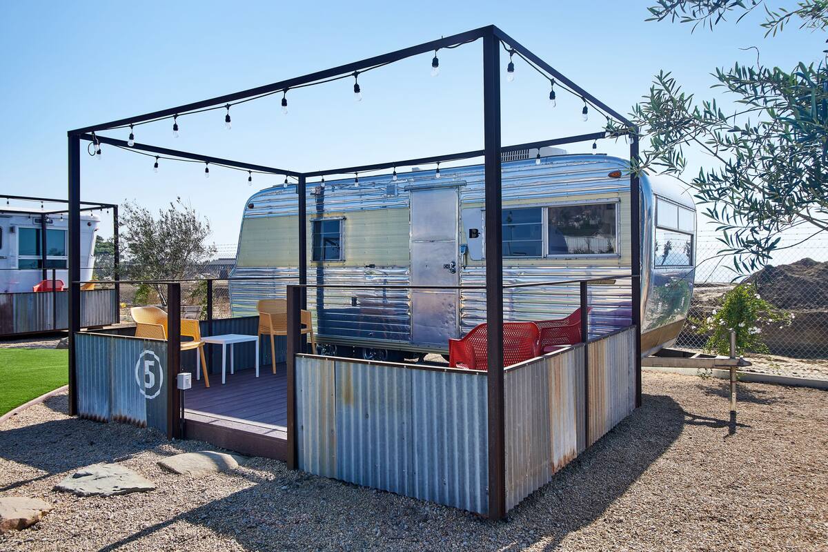 A recreational vehicle (RV) with a covered outdoor area featuring a table and chairs, surrounded by a metal fence.