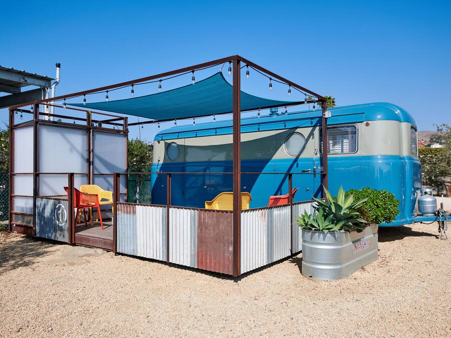 Uma carrinha camper azul com área de estar coberta no exterior, incluindo uma mesa e cadeiras.