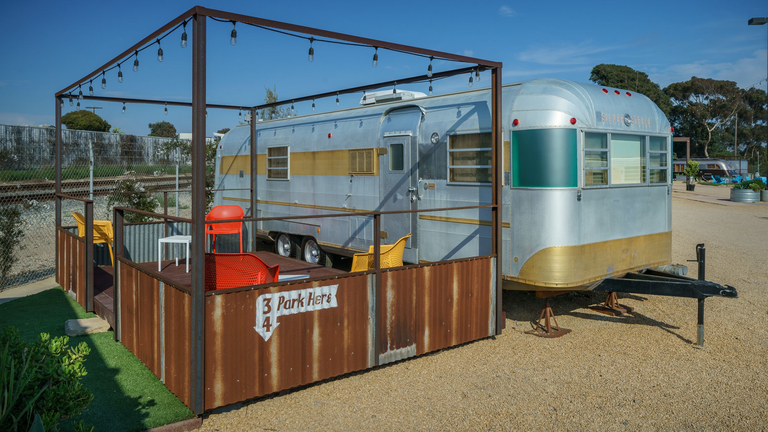 Una caravana vintage con un área cerrada pequeña que tiene una mesa y sillas, con la leyenda '3 Park Here 4'.