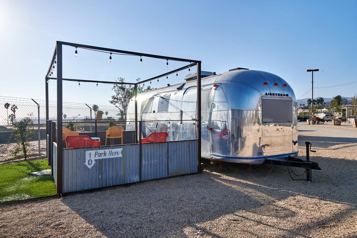 A vintage trailer with a 'Park Here' sign, a covered seating area, and a clear view of the surrounding area.