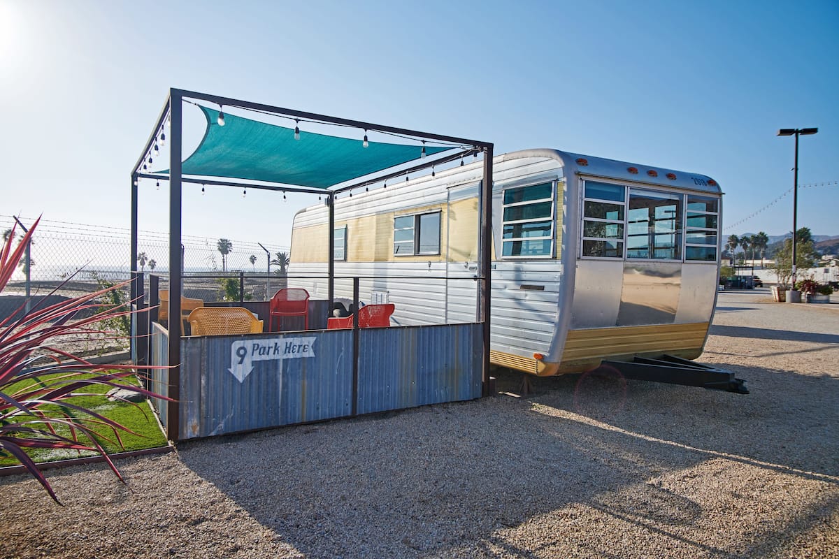 A vintage camper van parked next to a shaded picnic table with a sign reading "9 Park Here".