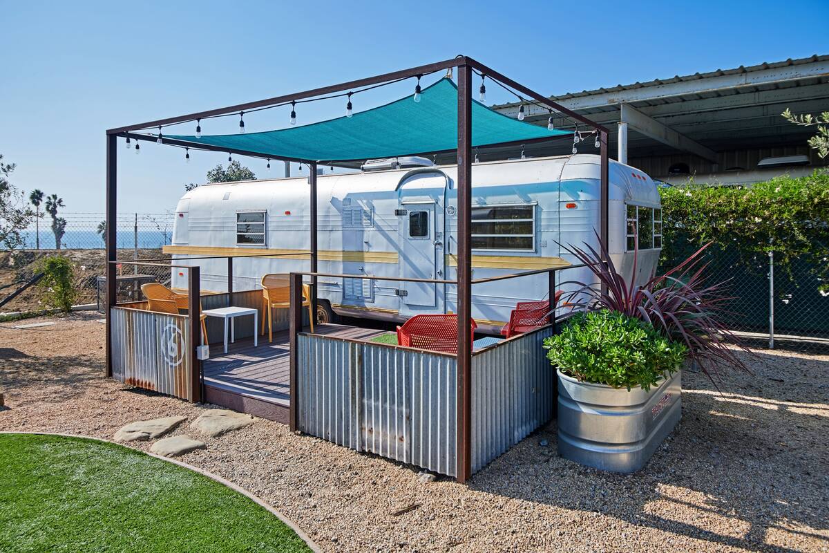 A recreational vehicle (RV) with a covered outdoor seating area, including a table and chairs, and a potted plant.