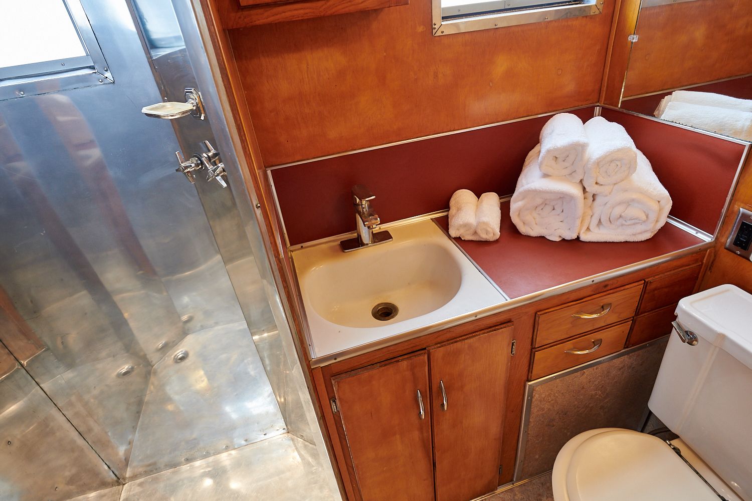 Un baño pequeño con lavamanos, espejo e inodoro. Hay toallas ordenadas sobre la encimera.
