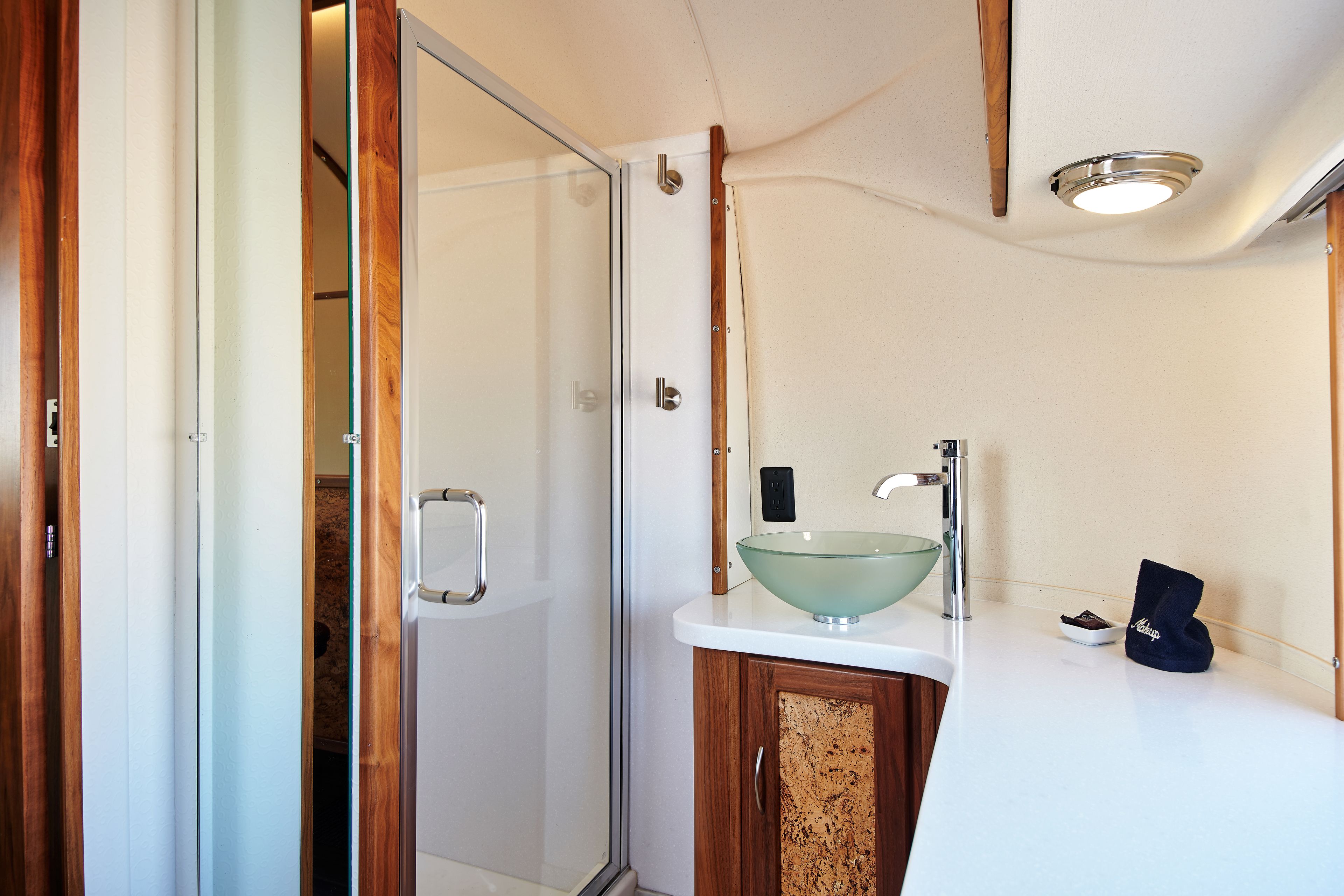 A modern bathroom with a glass shower enclosure, a white sink with a glass bowl, and a wooden cabinet.