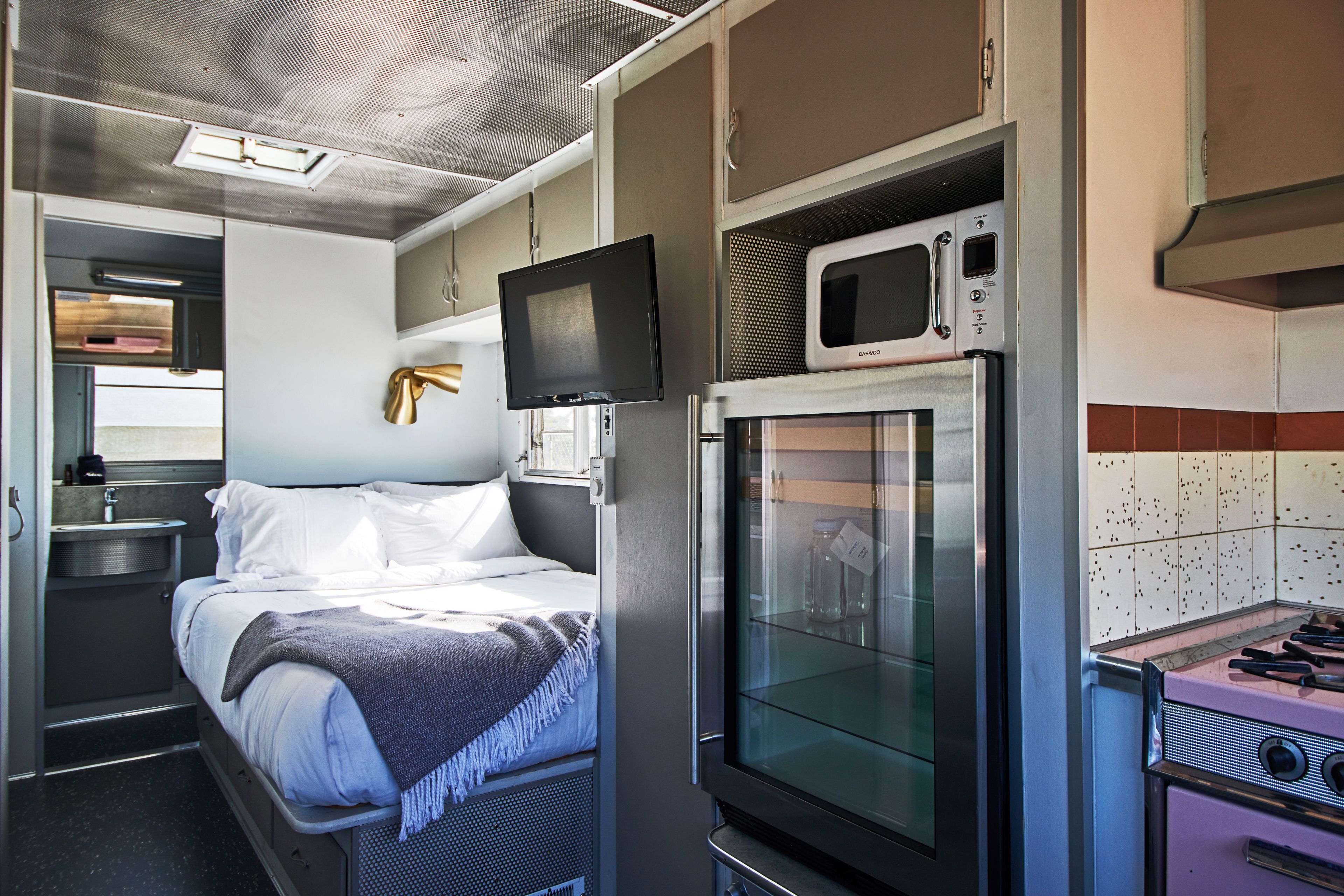 Una habitación funcional con cama, televisión, microondas y una pequeña cocina.
