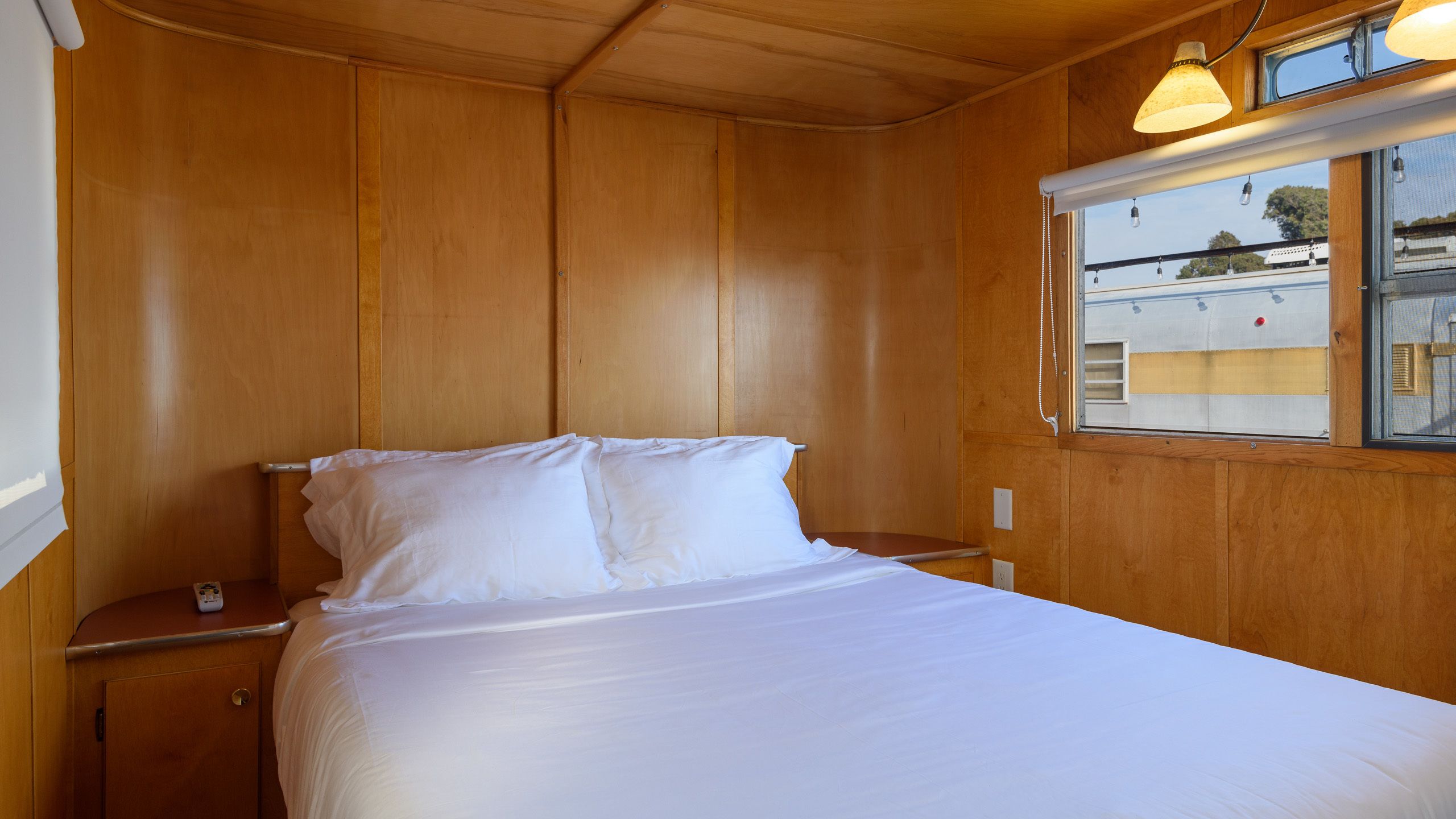 A single bed with white linens in a cabin with wooden walls and a window.