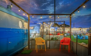 A covered outdoor seating area with a view of vintage trailers, string lights, and a wooden deck. - Waypoint Ventura (Ventura)