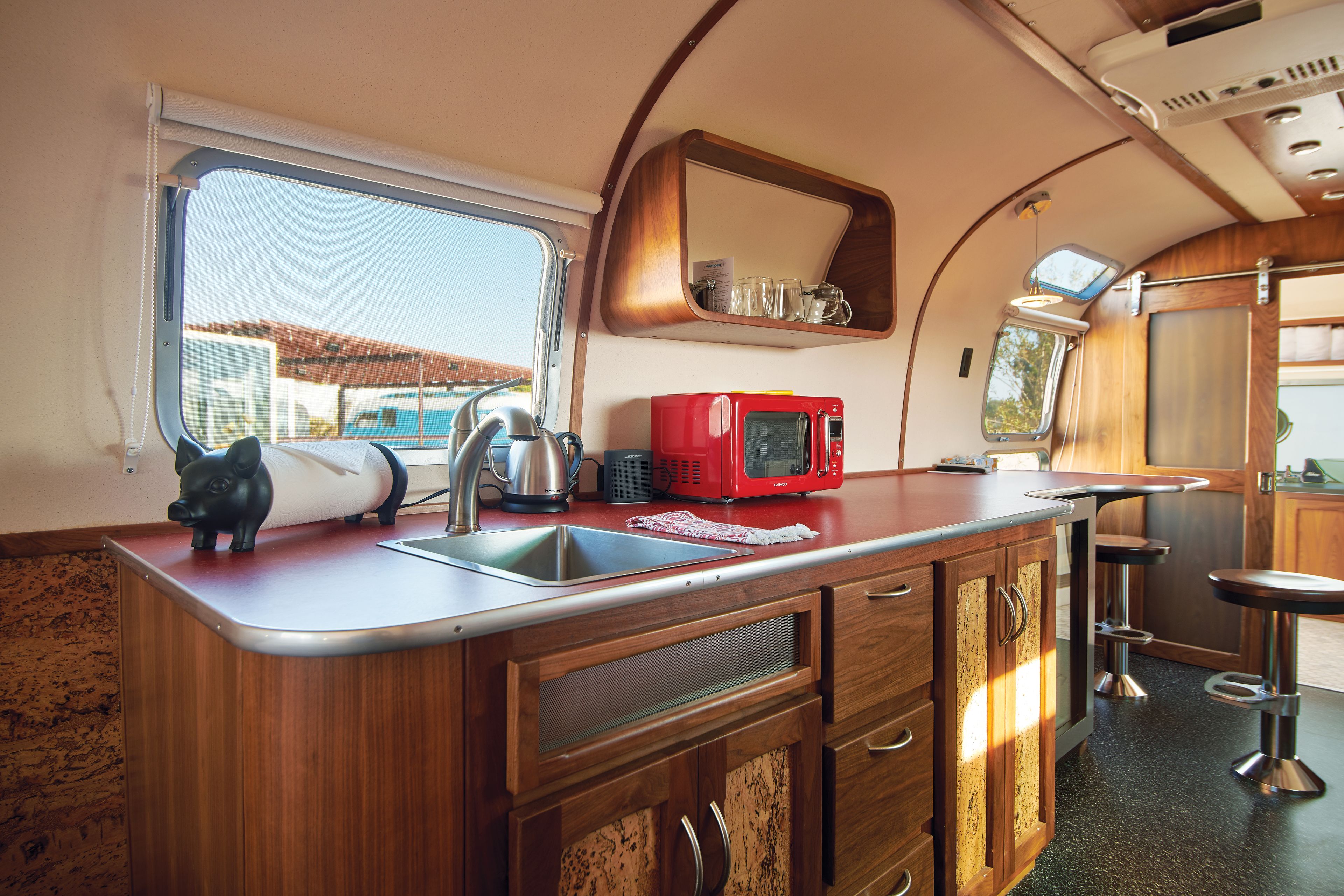 A compact kitchen with a sink, a red microwave, and a small window.