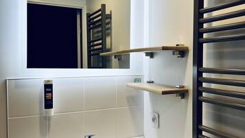 Un bagno con un lavandino bianco, uno specchio, un porta asciugamani e uno scaffale.