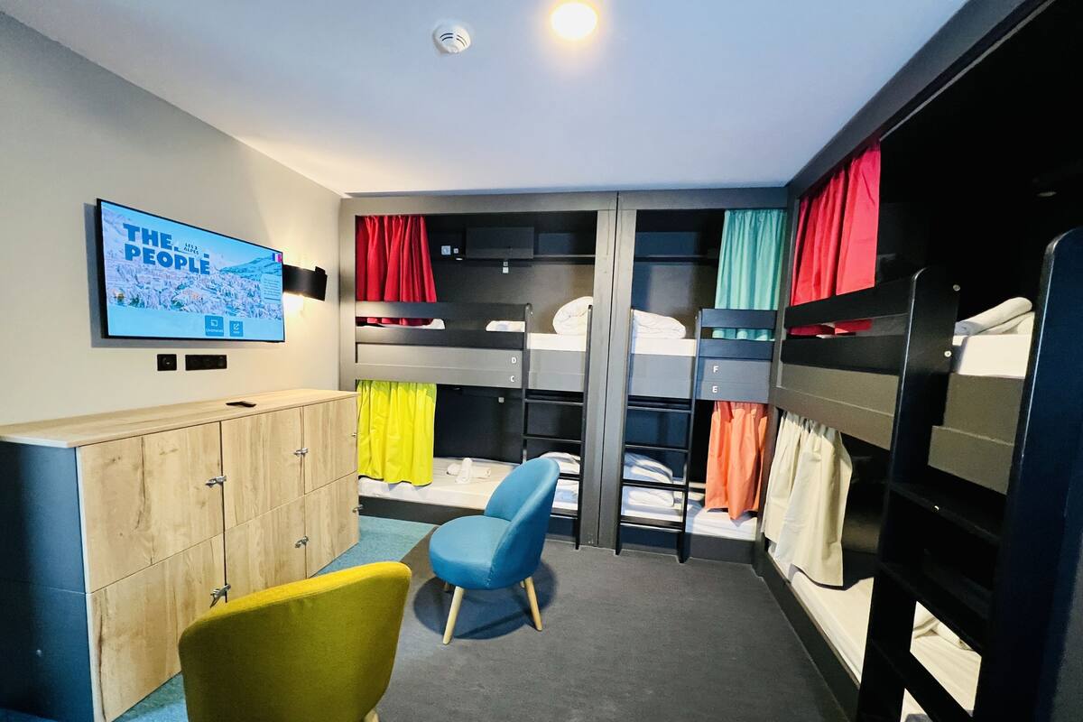 Une chambre avec des lits superposés, un téléviseur, une armoire en bois et une chaise bleue.