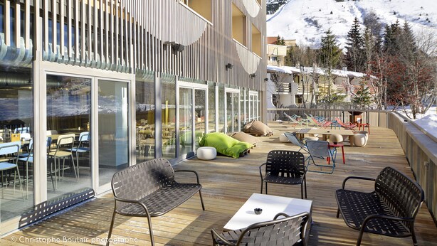 Een terras met buitenmeubilair, een glazen wand en uitzicht op een besneeuwde berg.