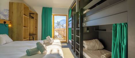 Habitació d'hotel amb un llit superposat, un armari de fusta i una finestra gran amb cortines.