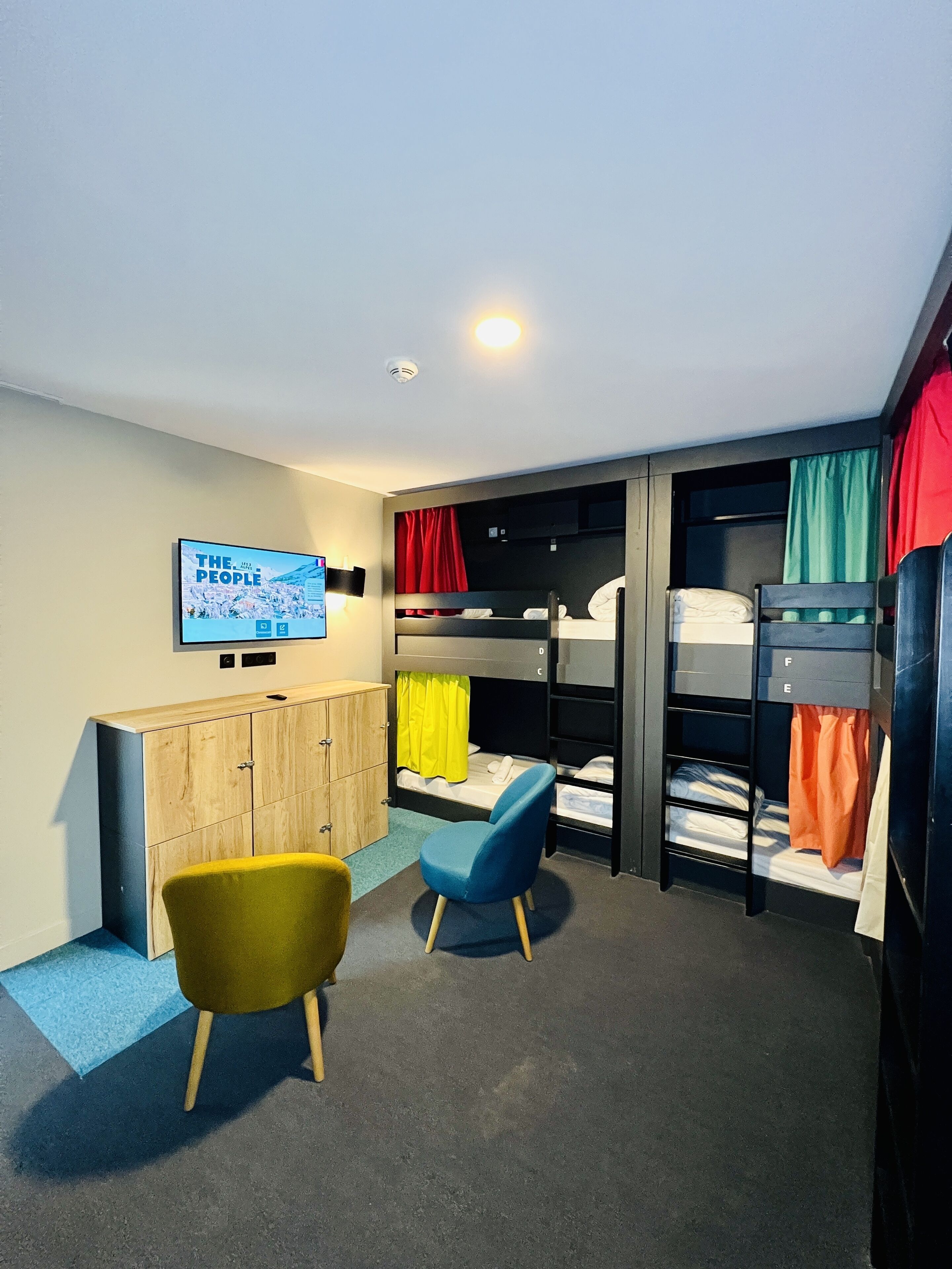 A room with bunk beds, a TV, a wooden cabinet, and two chairs.