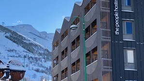 Een hotel met een modern design, met meerdere balkons en een skipiste op de achtergrond.