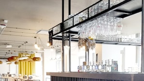 Een bar met krukken, een toonbank en glazen die hangen.