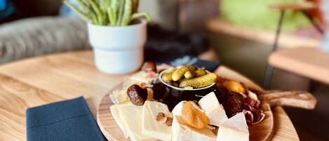 Uma mesa de madeira com uma tábua de queijos, azeitonas e picles.