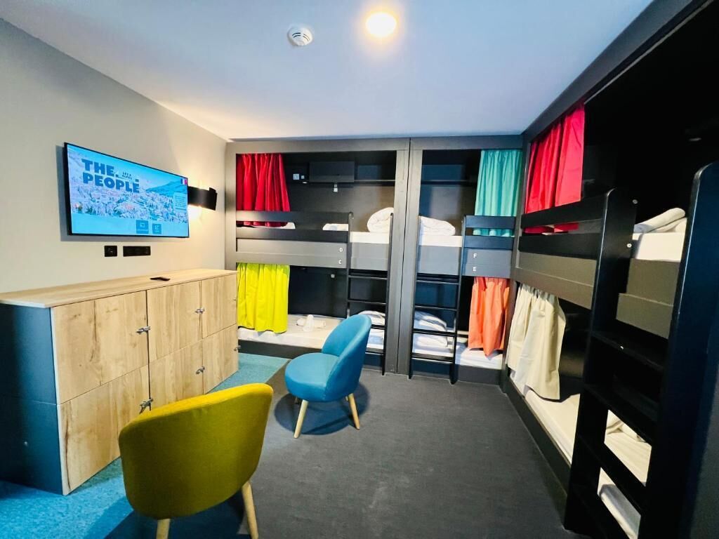 Un dormitorio con literas, un televisor, un armario de madera y una silla azul.