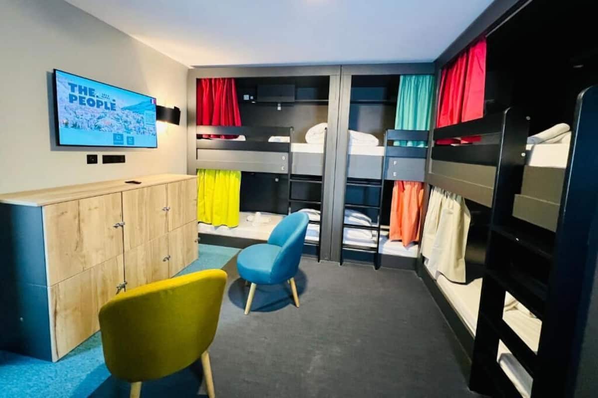 Une chambre avec des lits superposés, un téléviseur, une armoire en bois et une chaise bleue.