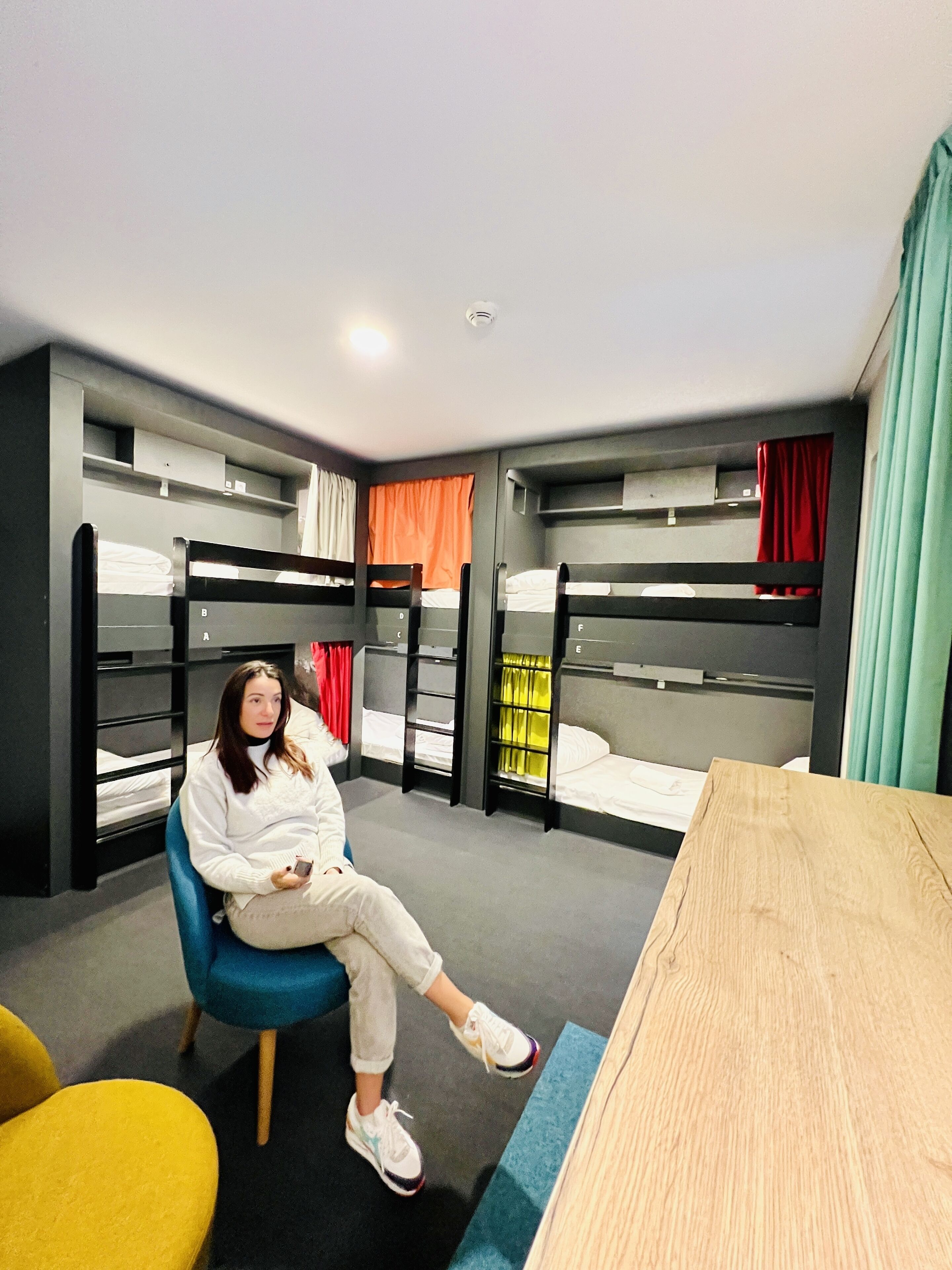 Ein Zimmer mit Etagenbetten, einem blauen Stuhl, einem Holztisch und einem gelben Stuhl.
