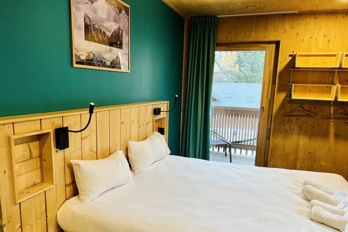 Une pièce aux murs lambrés, avec un lit, un tableau accroché au mur et un balcon doté d’une balustrade en bois.