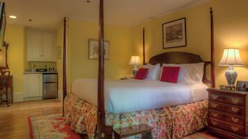 A four-poster bed with a floral bedspread, a wooden nightstand with a lamp, and a small table with a chair.