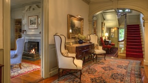 A grand entryway with a fireplace, elegant furniture, and a red carpet leading to a staircase. - Francis Malbone House Inn (Newport)