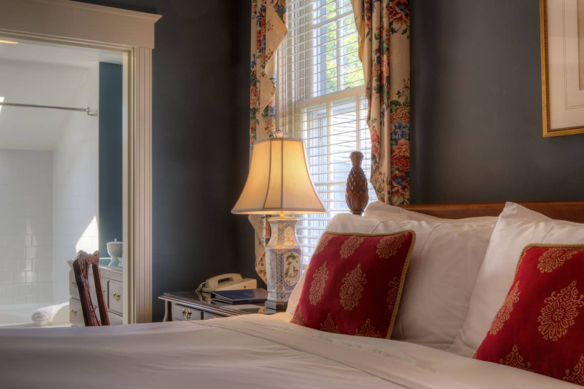 A hotel room with a bed, a nightstand, a lamp, and a window with curtains.