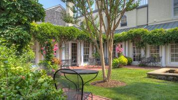 A courtyard with a brick patio, metal table and chairs, and a tree.