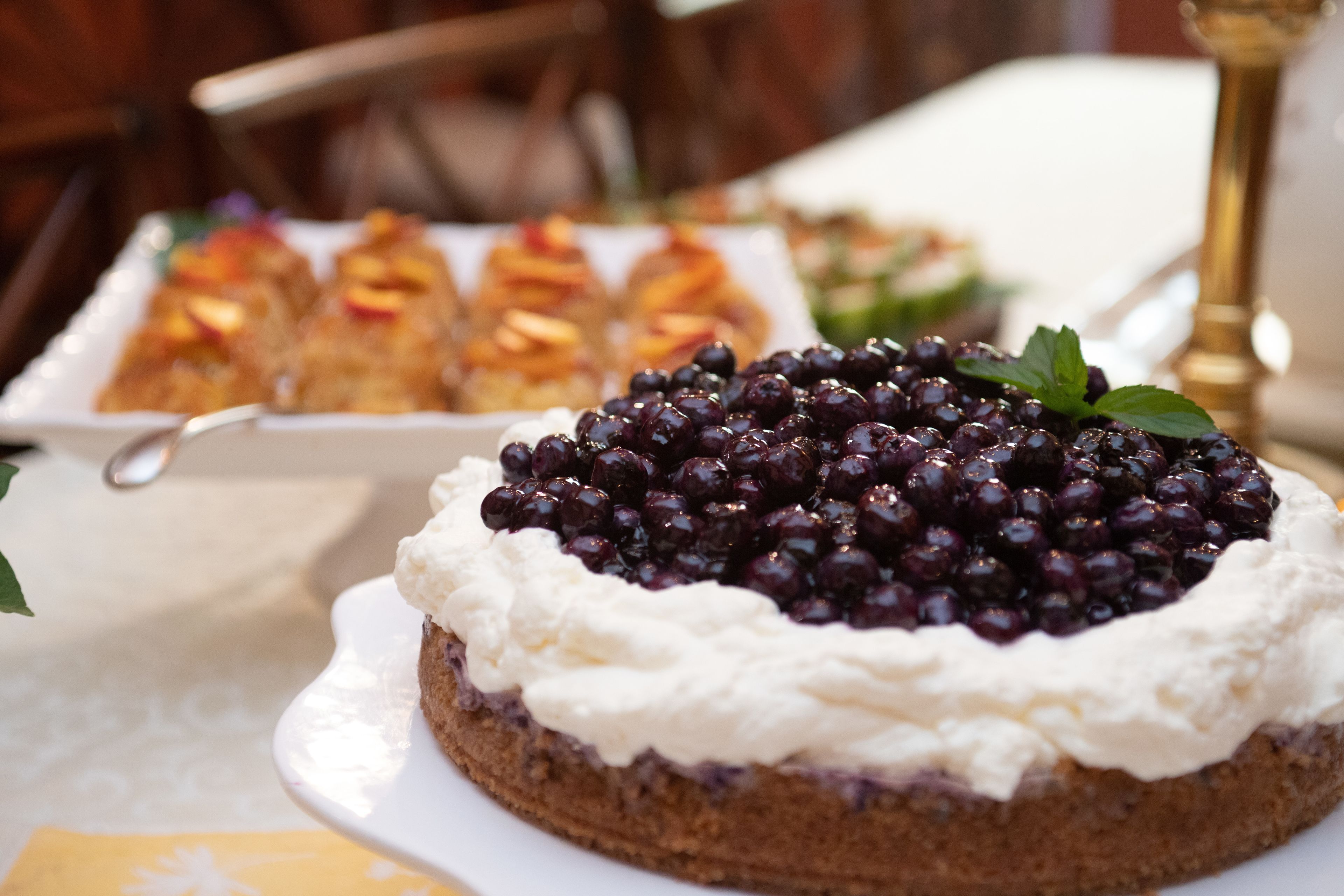 A dessert table with a cake topped with berries and whipped cream, and other pastries in the background.