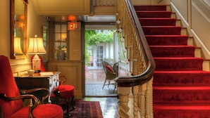 A grand staircase with red carpeted steps, a wooden chair with a red cushion, a desk with a lamp, and a door marked "EXIT". - Francis Malbone House Inn (Newport)